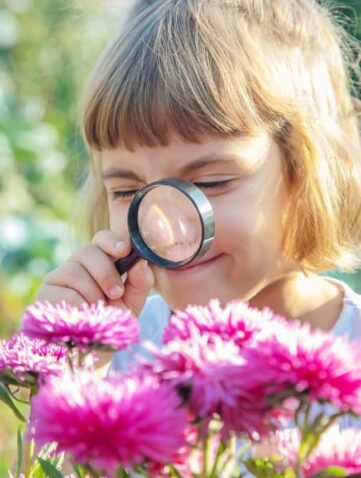 Meisje met vergrootglas bekijkt bloemen