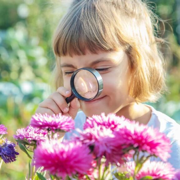 Meisje met vergrootglas bekijkt bloemen