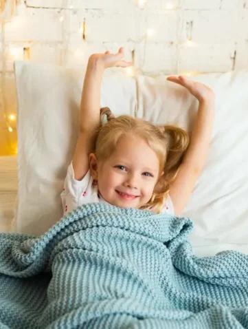 Meisje rekt zich uit in bed met blauwe sprei