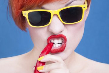 Vrouw met zonnebril bijt in een chilipeper