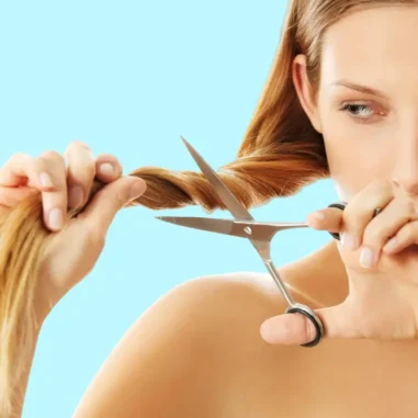 Vrouw knipt haar met schaar tegen blauwe achtergrond.