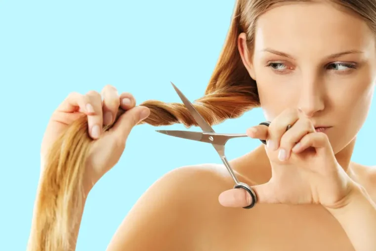 Vrouw knipt haar met schaar tegen blauwe achtergrond.