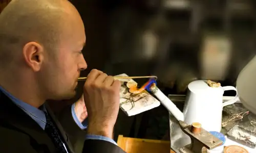 Goudsmid aan het werk met vlam en gereedschap.