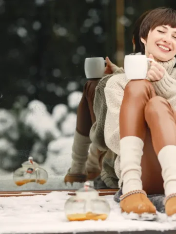 Vrouw met UGGs geniet van warme drank in de sneeuw.