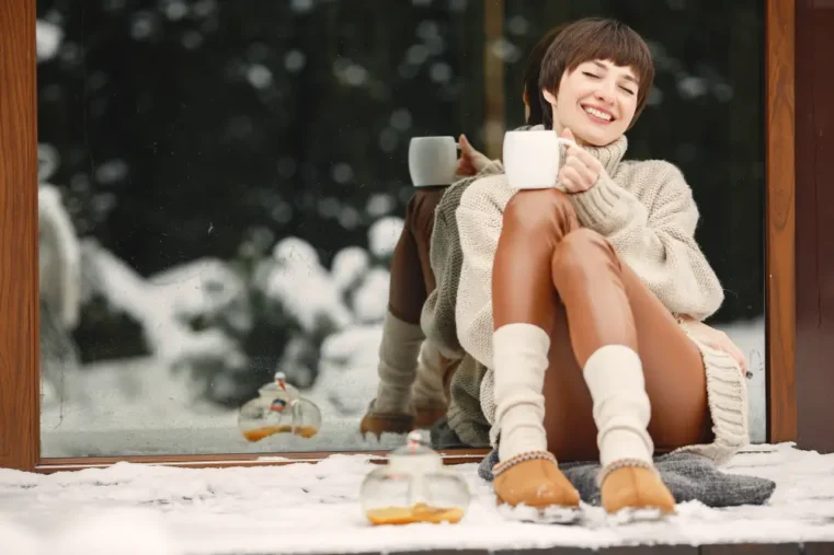 Vrouw met UGGs geniet van warme drank in de sneeuw.