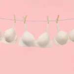 Drie witte beha's aan waslijn tegen roze achtergrond.