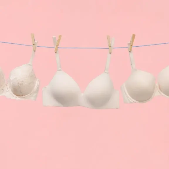 Drie witte beha's aan waslijn tegen roze achtergrond.