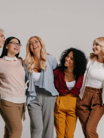 Groep lachende vrouwen van verschillende leeftijd samen in casual outfits.