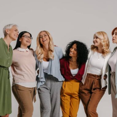 Groep lachende vrouwen van verschillende leeftijd samen in casual outfits.