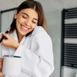 Vrouw met badjas, koffie en mobiele telefoon en make-up kwast