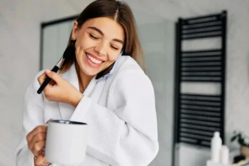 Vrouw met badjas, koffie en mobiele telefoon en make-up kwast