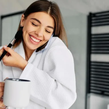 Vrouw met badjas, koffie en mobiele telefoon en make-up kwast