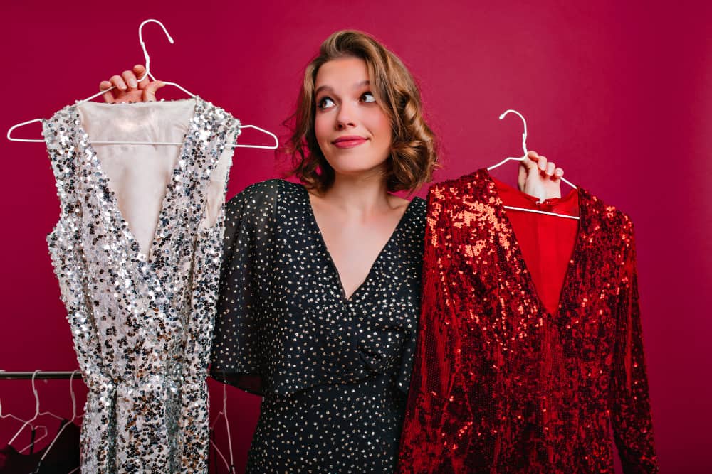 vrouw houdt twee verschillende jurken met glitters voor zich