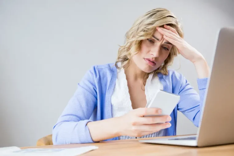 vrouw met bankpas achter laptop kijkt zorgelijk