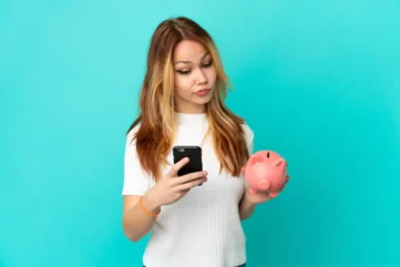Vrouw met mobiel in hand en spaarvarken in de andere hand