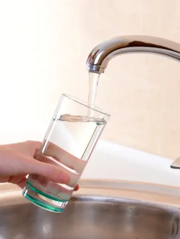 hand van vrouw met glas die water uit kraan tapt