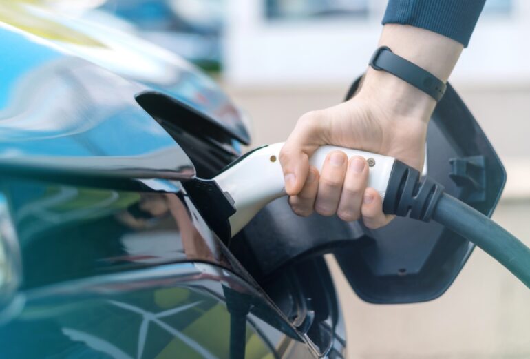 Hand steekt stekker in elektrische auto.