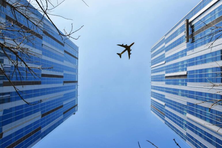 Vliegtuig boven hoge gebouwen met blauwe lucht.