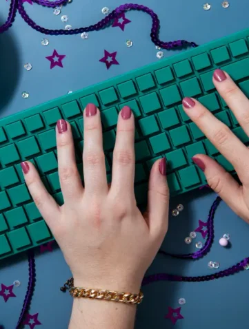 Handen typen op groen toetsenbord naast bakje popcorn.