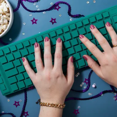 Handen typen op groen toetsenbord naast bakje popcorn.