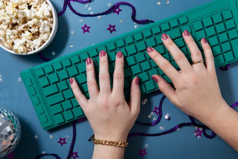 Handen typen op groen toetsenbord naast bakje popcorn.