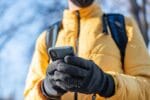 Persoon met verwarmde handschoenen die zijn mobiel bedient.