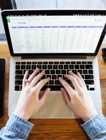 Twee handen werken op laptop met kop koffie bril en boekje