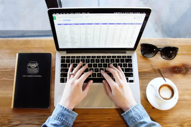Twee handen werken op laptop met kop koffie bril en boekje