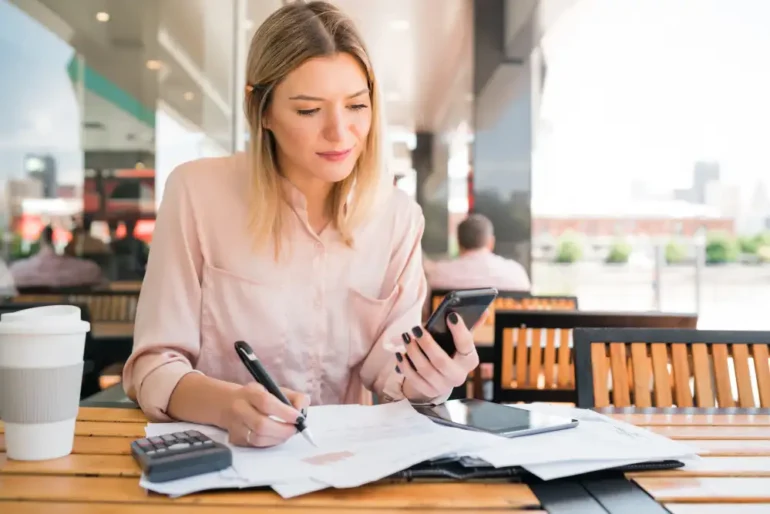 Vrouw doet administratie met rekenmachine en mobiel