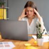 vrouw zit achter laptop met hoofdpijn