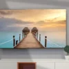 Grote TV in woonkamer met beeld van zonsondergang bij pier over oceaan