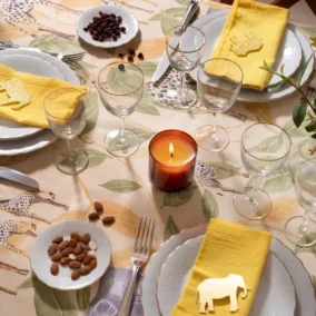 Gedekte tafel met tafelzeil, kaars, gele servetten en borden.