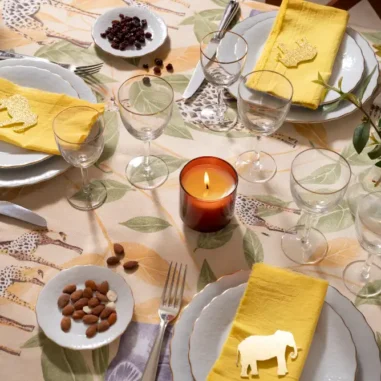 Gedekte tafel met tafelzeil, kaars, gele servetten en borden.