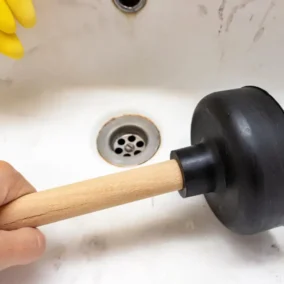 Hevel ontstoppen gootsteen met zuignap en gele handschoenen.