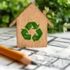 Houten huisje met recycling-symbool op bouwtekening.