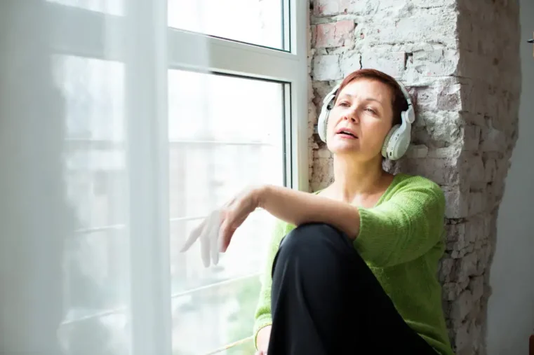 Vrouw met ontspant met koptelefoon bij raam.