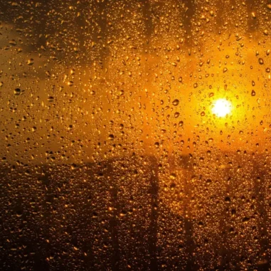 Regen op raam met zonsondergang op achtergrond.