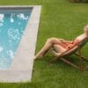 Vrouw zit op luie stoel in het gras aan rand van zwembad