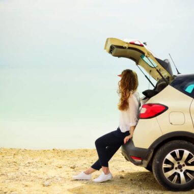 vrouw zit in achterklep van auto en kijkt naar de zee