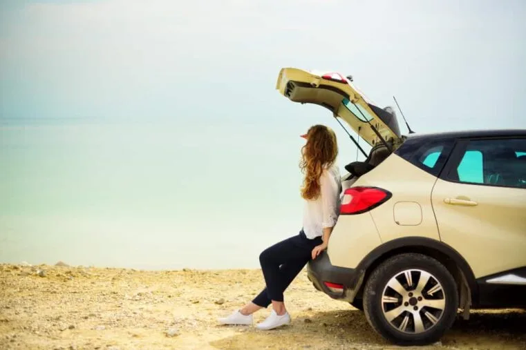 vrouw zit in achterklep van auto en kijkt naar de zee