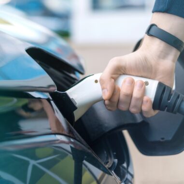 Hand steekt stekker in elektrische auto.