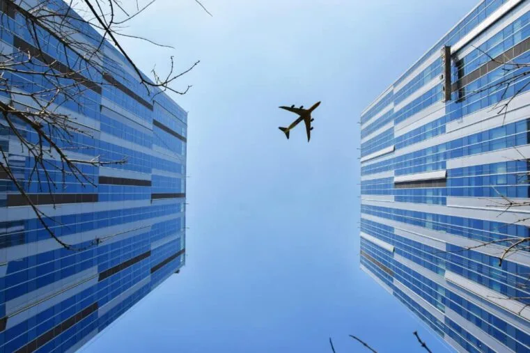 Vliegtuig boven hoge gebouwen met blauwe lucht.